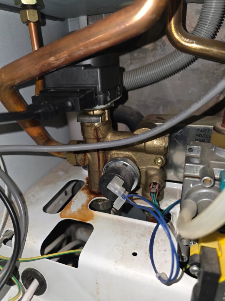 Close-up inside a gas boiler showing the brass diverter valve, gas valve and pipework during a repair